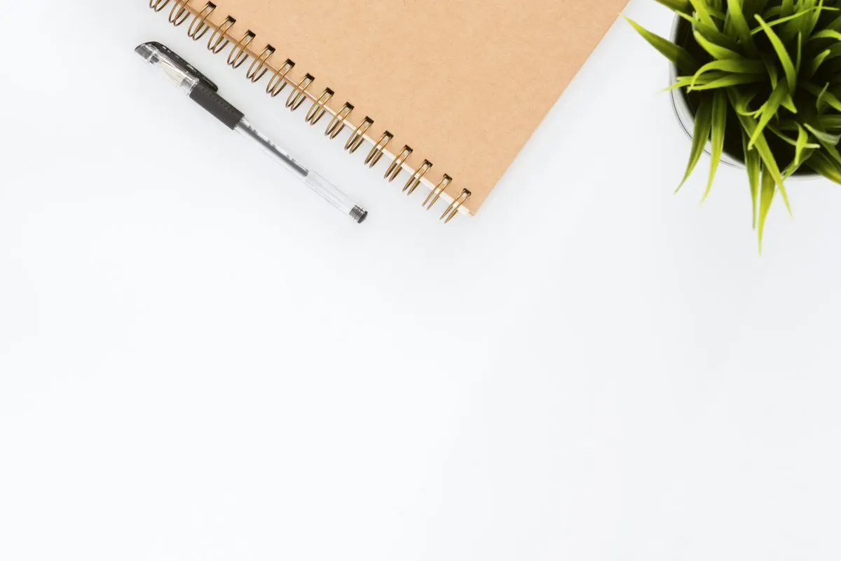 Caderno aberto com caneta e uma pequena planta sobre a mesa